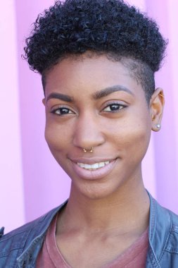 Mor duvar arkasında kısa kıvırcık saçlı güzel bir Afrikalı kadının yakın plan portresi. 