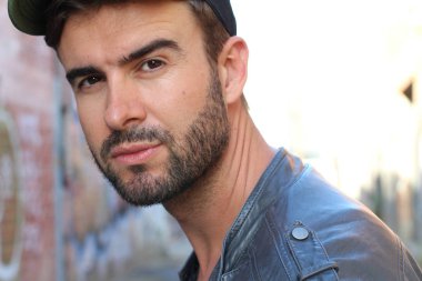 Genç, çekici bir hippi ve modaya uygun görünüşlü bir adam gülümsüyor. Mutlu pozlar veriyor. Gayri resmi giyiniyor, beysbol şapkası ve sakal takıyor.