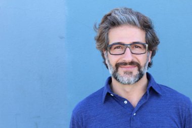 Mavi duvarın önündeki yakışıklı yetişkin adamın yakın plan portresi.