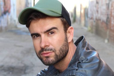 Genç, çekici bir hippi ve modaya uygun görünüşlü bir adam gülümsüyor. Mutlu pozlar veriyor. Gayri resmi giyiniyor, beysbol şapkası ve sakal takıyor.