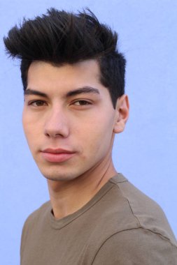 Mavi duvarın önünde poz veren yakışıklı genç adamın yakın plan portresi.