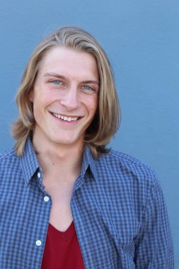 Mavi duvarın önünde uzun sarı saçlı yakışıklı genç adamın yakın plan portresi.