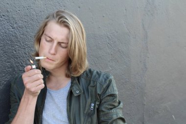 Sokakta sigara içen uzun saçlı yakışıklı bir adamın yakın plan portresi.