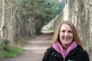 Güler yüzlü sarışın kadın güz parkında gündüz vakti duruyor.