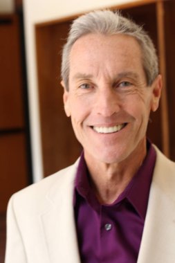 Bej ceketli yakışıklı olgun bir adamın kameraya bakarken yakın plan portresi.