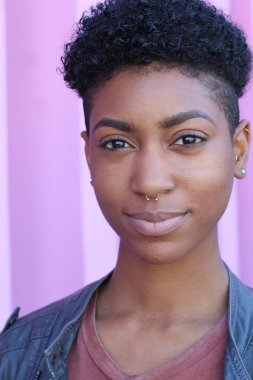 Mor duvar arkasında kısa kıvırcık saçlı güzel bir Afrikalı kadının yakın plan portresi. 