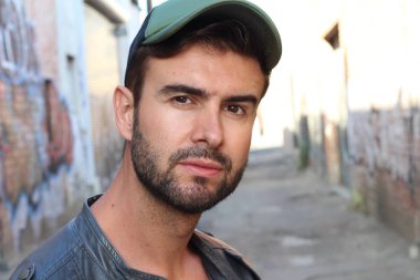 Genç, çekici bir hippi ve modaya uygun görünüşlü bir adam gülümsüyor. Mutlu pozlar veriyor. Gayri resmi giyiniyor, beysbol şapkası ve sakal takıyor.