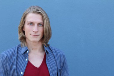 Mavi duvarın önünde uzun sarı saçlı yakışıklı genç adamın yakın plan portresi.