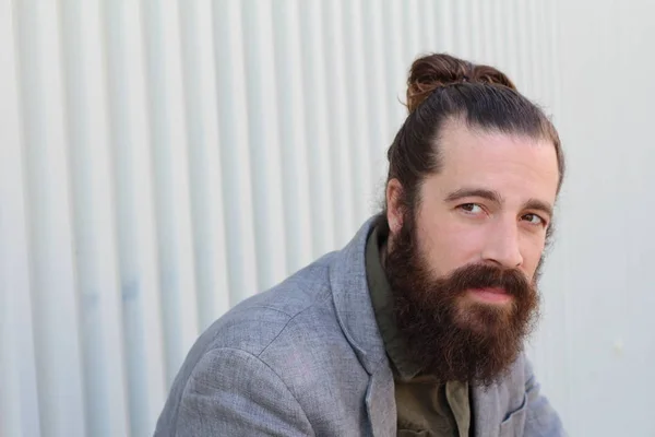 Stylish bearded hipster model with man bun hairstyle, lifestyle in the street, depth of field