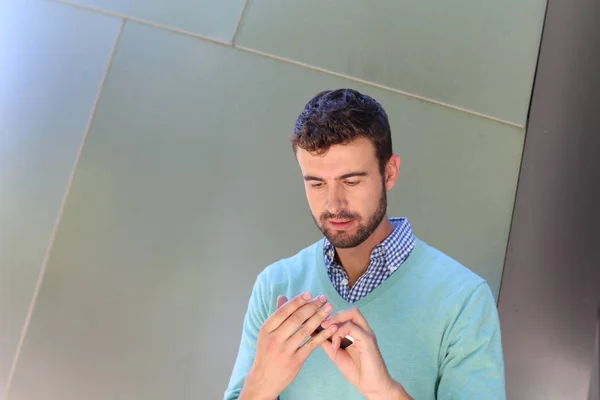 Portrait of young man in checked shirt and cyan sweater talking on phone