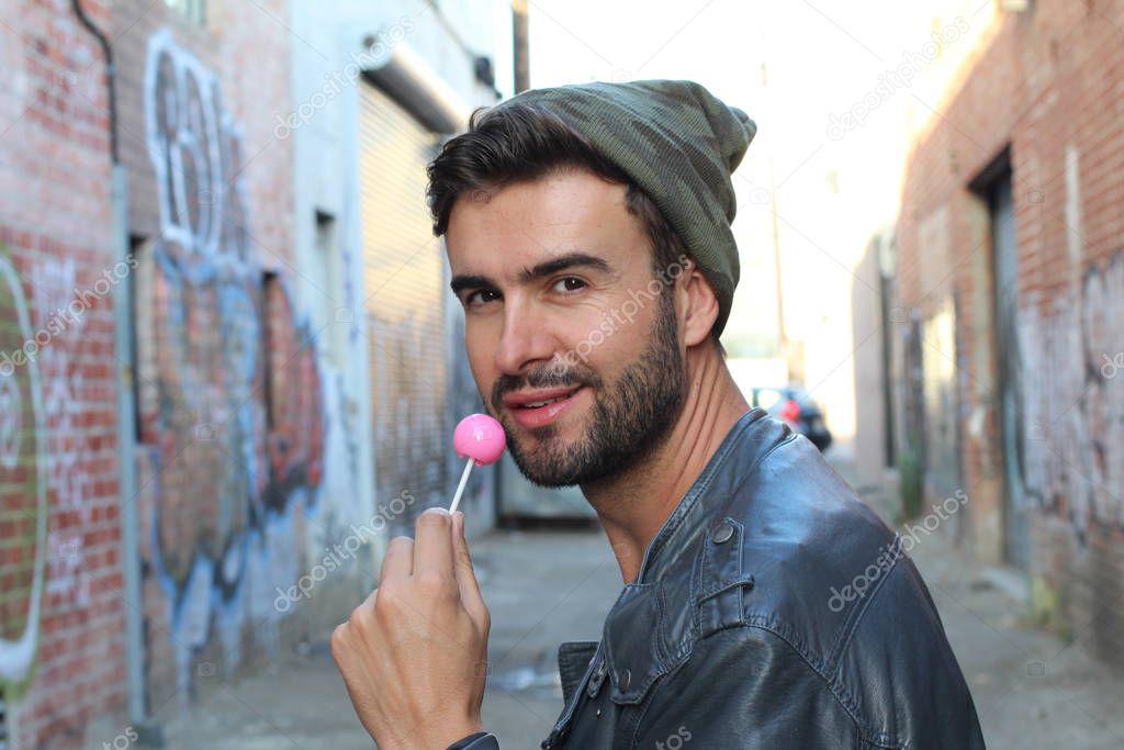 Outdoor fashionable lifestyle creative photo of a playful guy with a colorful lollipop