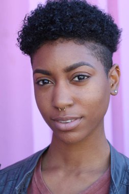 Mor duvar arkasında kısa kıvırcık saçlı güzel bir Afrikalı kadının yakın plan portresi. 