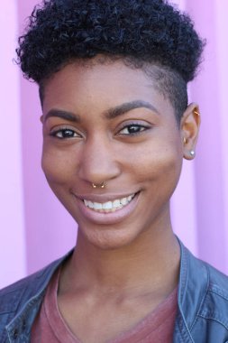 Mor duvar arkasında kısa kıvırcık saçlı güzel bir Afrikalı kadının yakın plan portresi. 