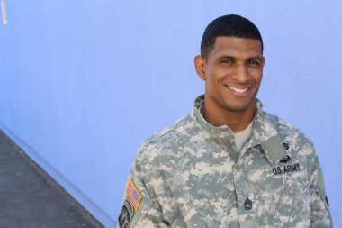 Mavi duvarın önünde üniformalı yakışıklı Afro-Amerikan askerinin yakın plan portresi