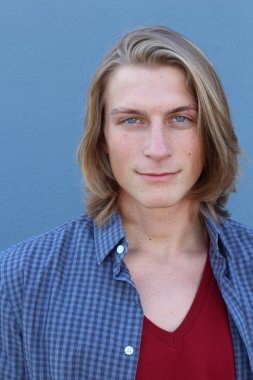 Mavi duvarın önünde uzun sarı saçlı yakışıklı genç adamın yakın plan portresi.