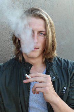 Sokakta sigara içen uzun saçlı yakışıklı bir adamın yakın plan portresi.