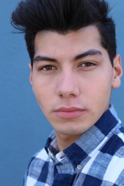 Mavi duvarın önünde poz veren yakışıklı genç adamın yakın plan portresi.