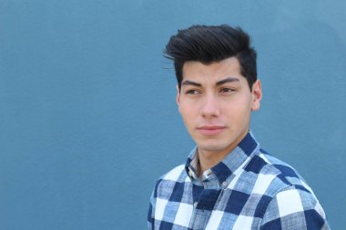 Mavi duvarın önünde poz veren yakışıklı genç adamın yakın plan portresi.