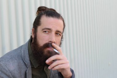 Sigara içen yakışıklı sakallı adamın portresi. Erkek saçı olan hippi..