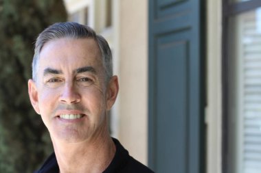 Siyah gömlekli yakışıklı olgun bir adamın yakın plan portresi. Sokakta kameraya bakıyor.