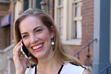 Güzel, güler yüzlü bir sarışın şehir dışında telefonla konuşuyor. 