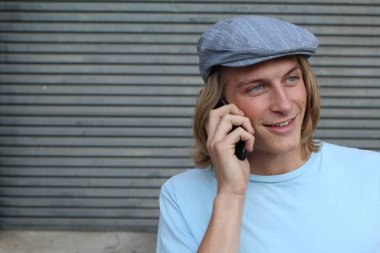 Sokakta telefonla konuşan, uzun saçlı, yakışıklı bir genç adamın yakın plan portresi.