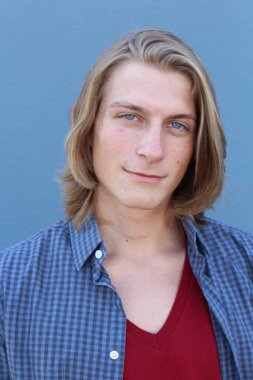 Mavi duvarın önünde uzun saçlı yakışıklı ve şık bir adamın yakın plan portresi.