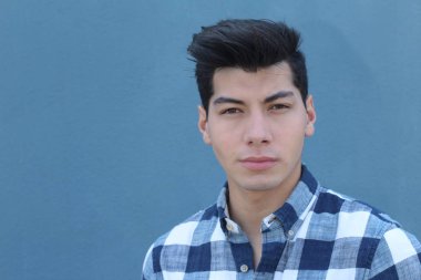 Mavi duvarın önündeki ekose gömlekli yakışıklı genç adamın yakın plan portresi.