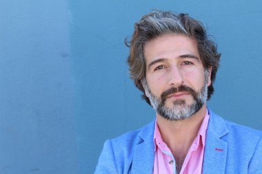 Mavi takım elbiseli ve mavi gömlekli yakışıklı bir iş adamının mavi duvarın önünde yakın plan portresi.