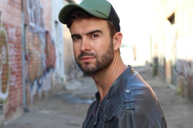 Genç, çekici bir hippi ve modaya uygun görünüşlü bir adam gülümsüyor. Mutlu pozlar veriyor. Gayri resmi giyiniyor, beysbol şapkası ve sakal takıyor.