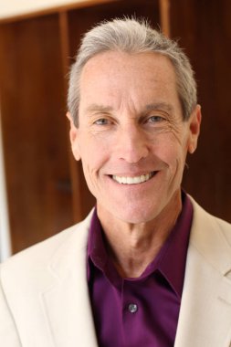 Bej ceketli yakışıklı olgun bir adamın kameraya bakarken yakın plan portresi.