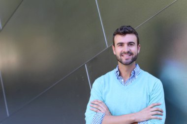 İşaretli gömlekli genç bir adam portresi ve kolları çapraz duran cyan süveter.