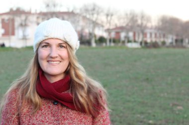 Kış giysileri içinde gülen sarışın kadının portresi gündüz vakti parkta duruyor.