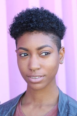 Mor duvar arkasında kısa kıvırcık saçlı güzel bir Afrikalı kadının yakın plan portresi. 