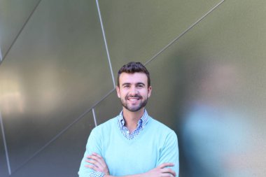 İşaretli gömlekli genç bir adam portresi ve kolları çapraz duran cyan süveter.