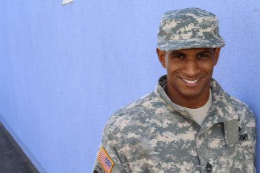 Mavi duvarın önünde üniformalı yakışıklı Afro-Amerikan askerinin yakın plan portresi