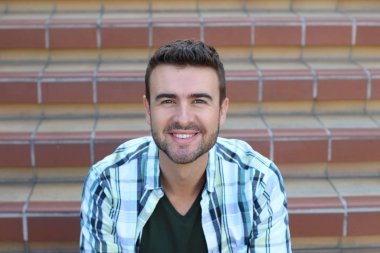 Ekose gömlekli, merdivenlerde oturan yakışıklı genç adamın yakın plan portresi.