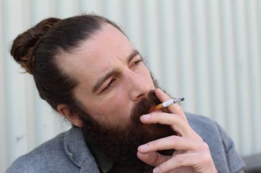 Sigara içen yakışıklı sakallı adamın portresi. Erkek saçı olan hippi..