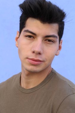 Mavi duvarın önünde poz veren yakışıklı genç adamın yakın plan portresi.