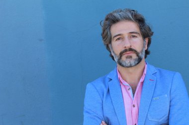 Mavi takım elbiseli ve mavi gömlekli yakışıklı bir iş adamının mavi duvarın önünde yakın plan portresi.