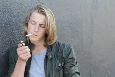 Sokakta sigara içen uzun saçlı yakışıklı bir adamın yakın plan portresi.