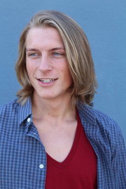 Mavi duvarın önünde uzun sarı saçlı yakışıklı genç adamın yakın plan portresi.