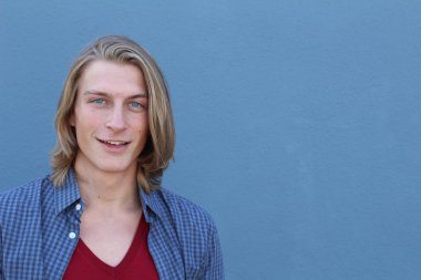 Mavi duvarın önünde uzun sarı saçlı yakışıklı genç adamın yakın plan portresi.