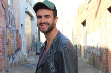 Genç, çekici bir hippi ve modaya uygun görünüşlü bir adam gülümsüyor. Mutlu pozlar veriyor. Gayri resmi giyiniyor, beysbol şapkası ve sakal takıyor.