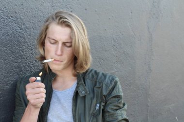 Sokakta sigara içen uzun saçlı yakışıklı bir adamın yakın plan portresi.