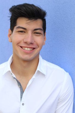 Mavi duvarın önünde poz veren yakışıklı genç adamın yakın plan portresi.