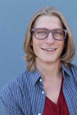 Mavi duvarın önünde uzun saçlı yakışıklı ve şık bir adamın yakın plan portresi.