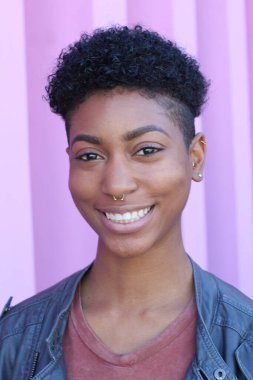 Mor duvar arkasında kısa kıvırcık saçlı güzel bir Afrikalı kadının yakın plan portresi. 