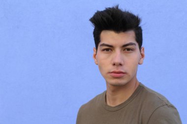 Mavi duvarın önünde poz veren yakışıklı genç adamın yakın plan portresi.