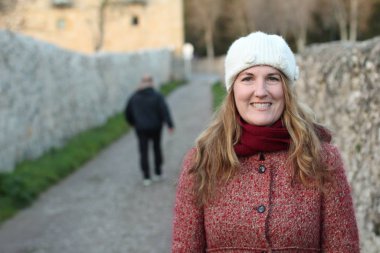 Kış giysileri içinde gülen sarışın kadının portresi gündüz vakti parkta duruyor.